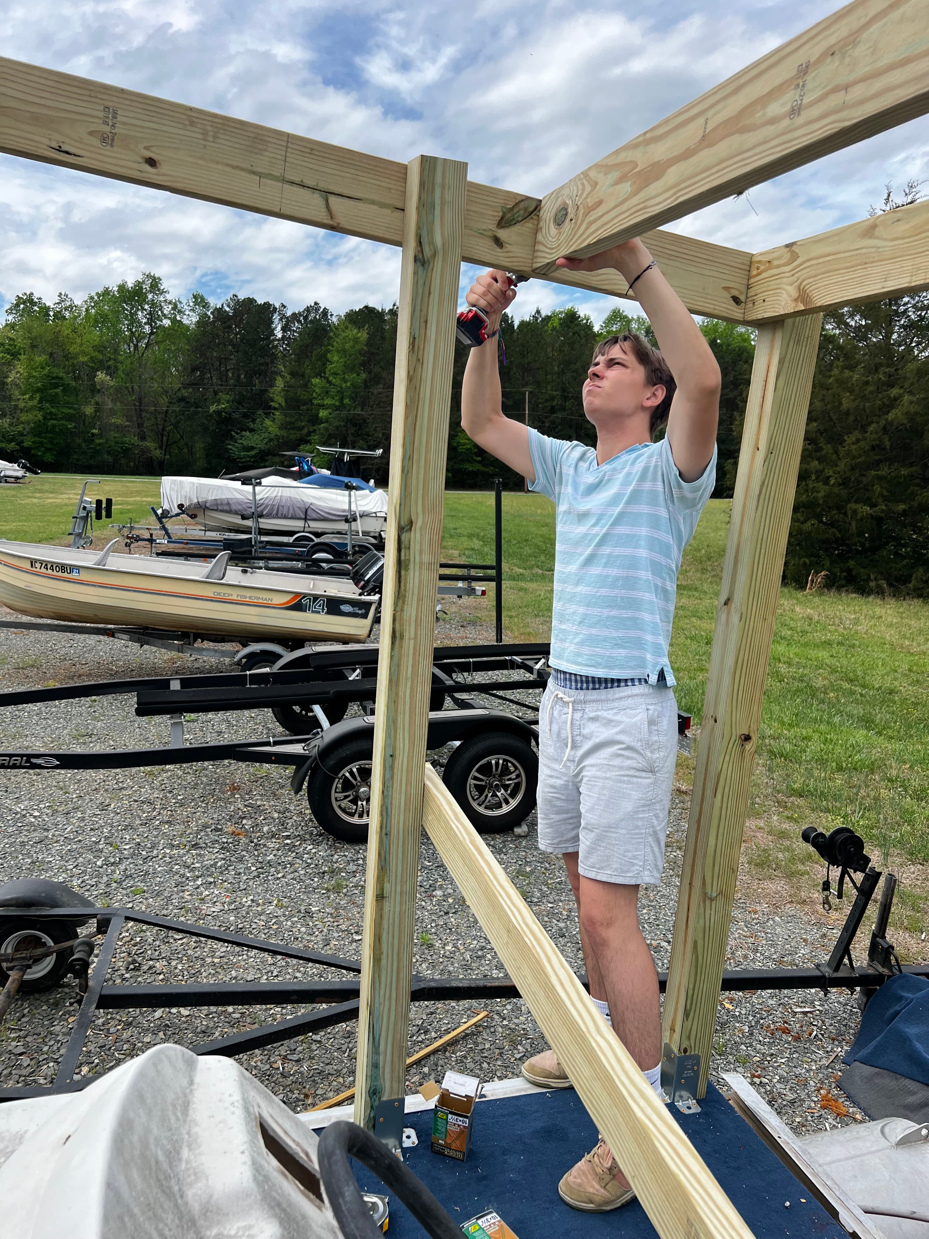 Person drilling into roof frame in boatyard with other boats in background