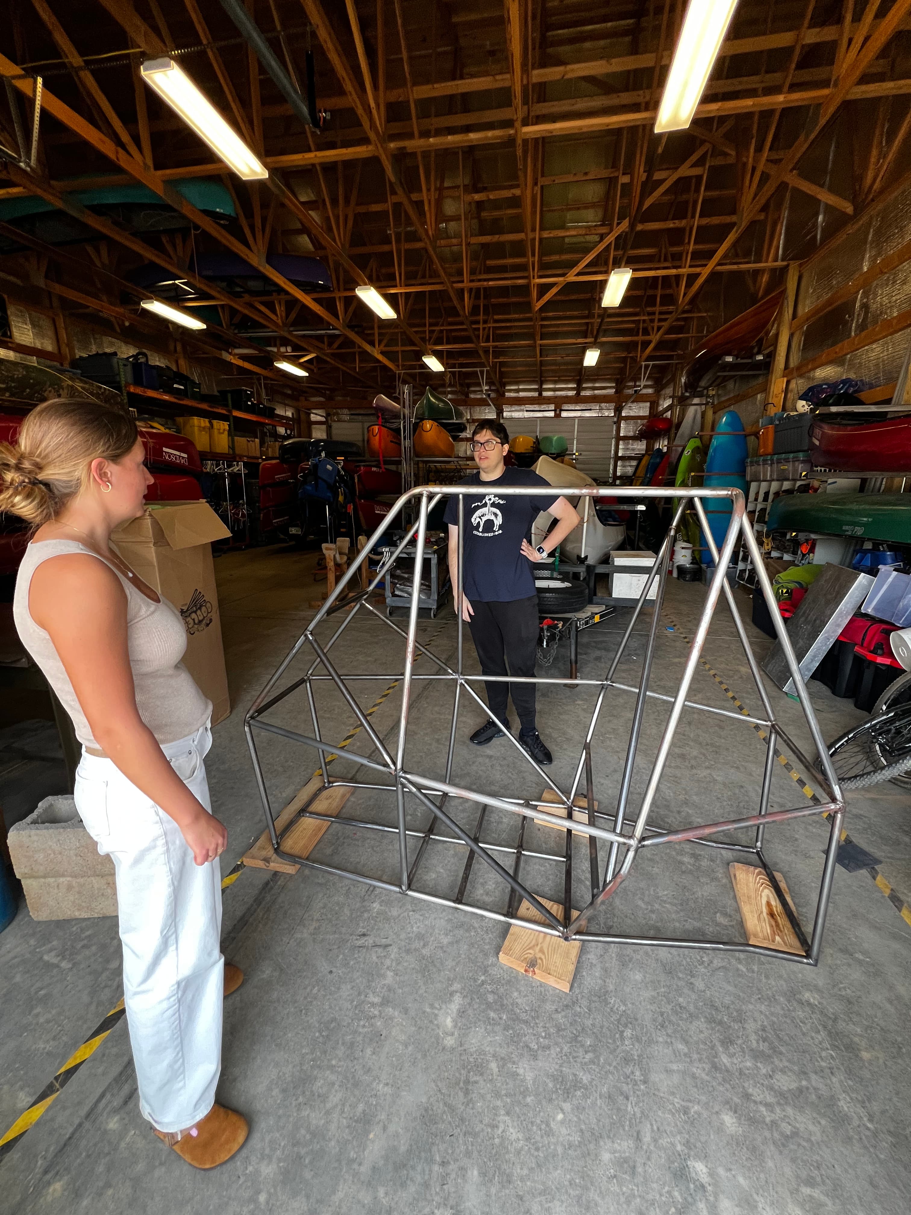 Bare welded chassis frame with two people examining it in the Lake Campus boathouse