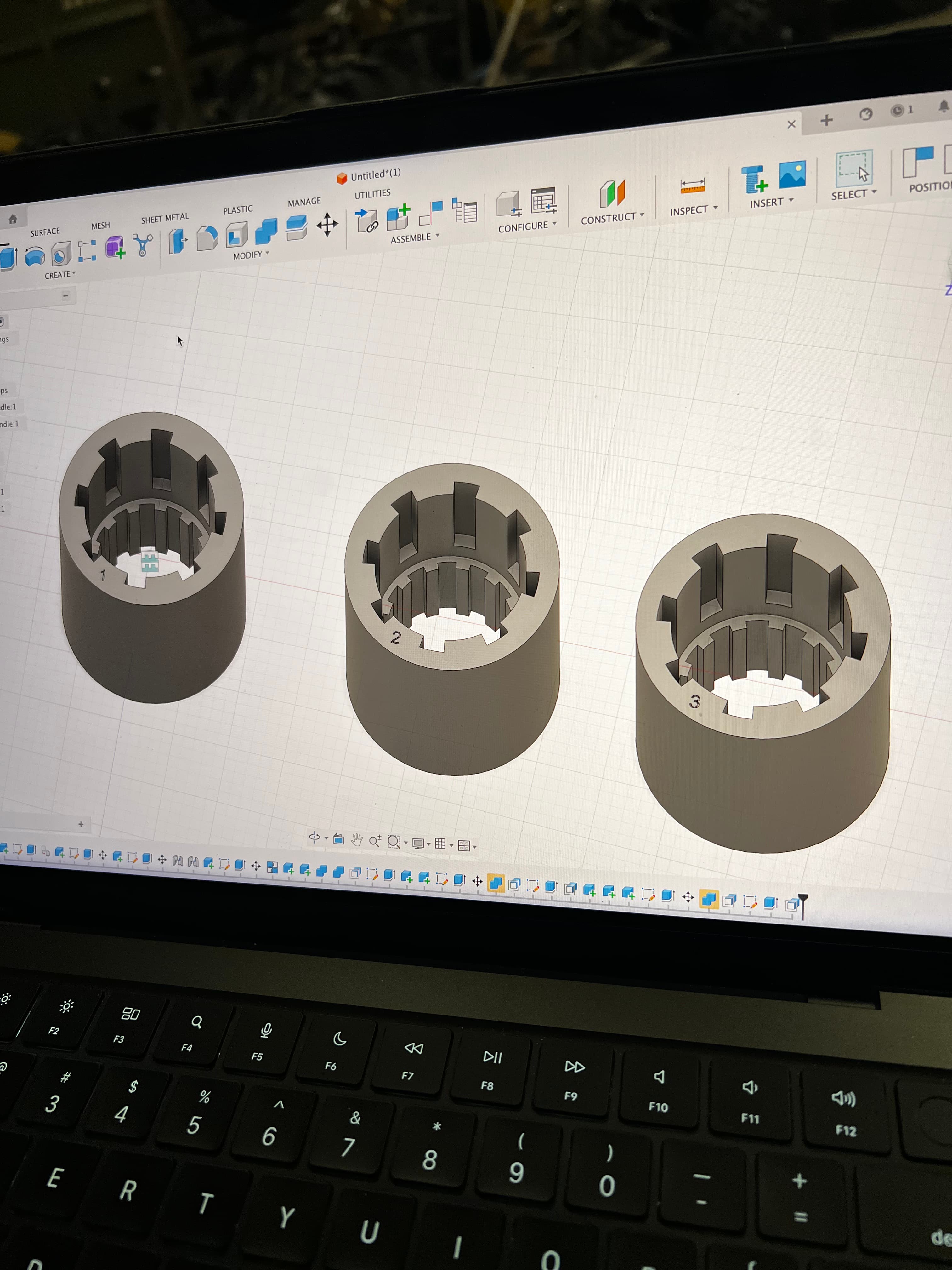 Laptop showing Fusion 360 with three numbered spindle adapter variants on screen