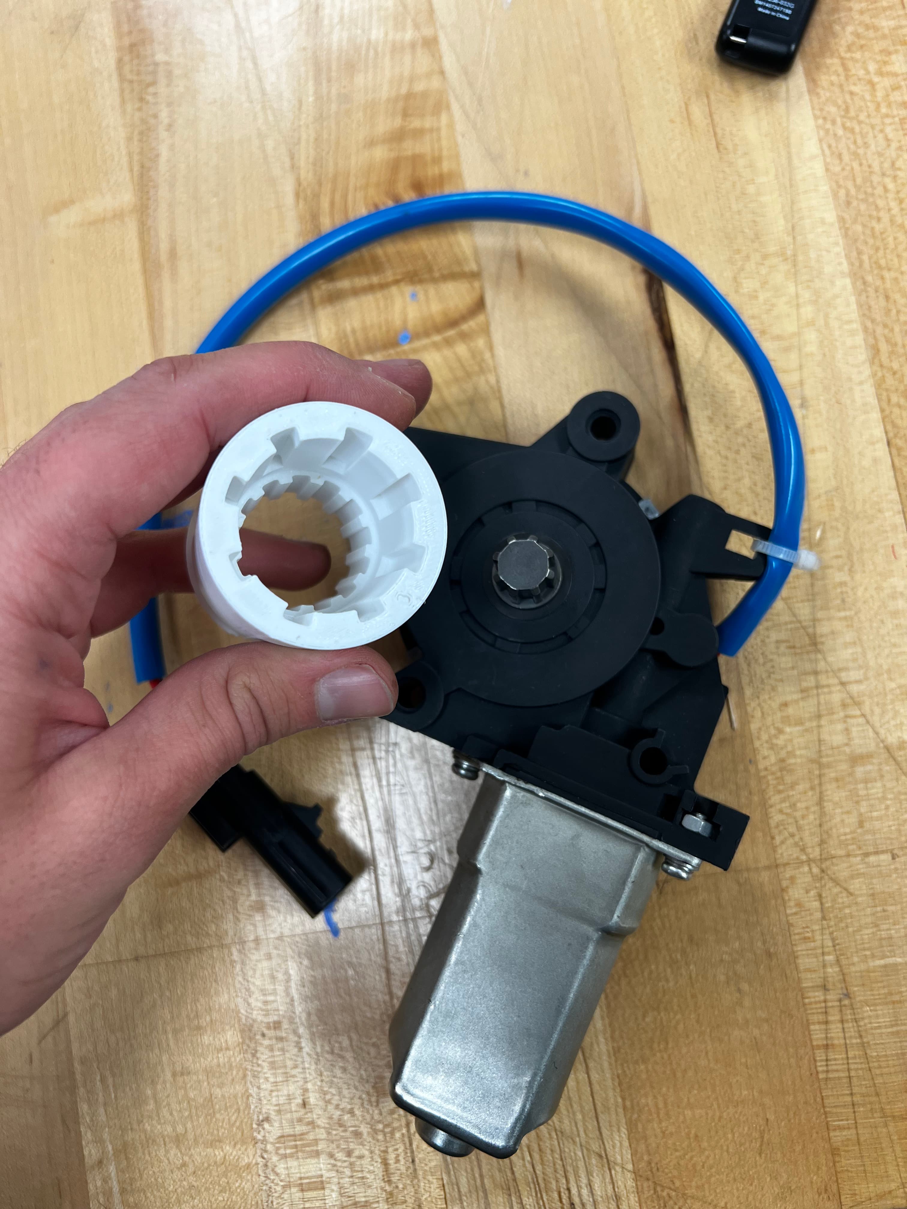 Hand holding a 3D-printed white spindle adapter next to the motor